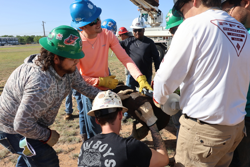 Lineworker students align utility pole hardware while classmates assist nearby.