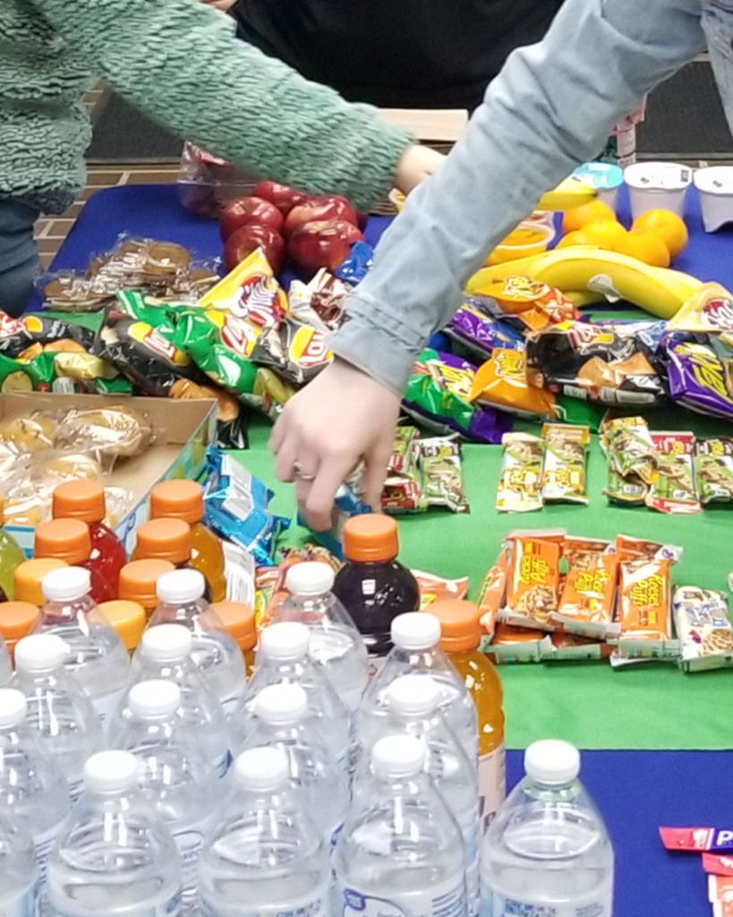 Hands pick up items from a table full of snacks and drinks.