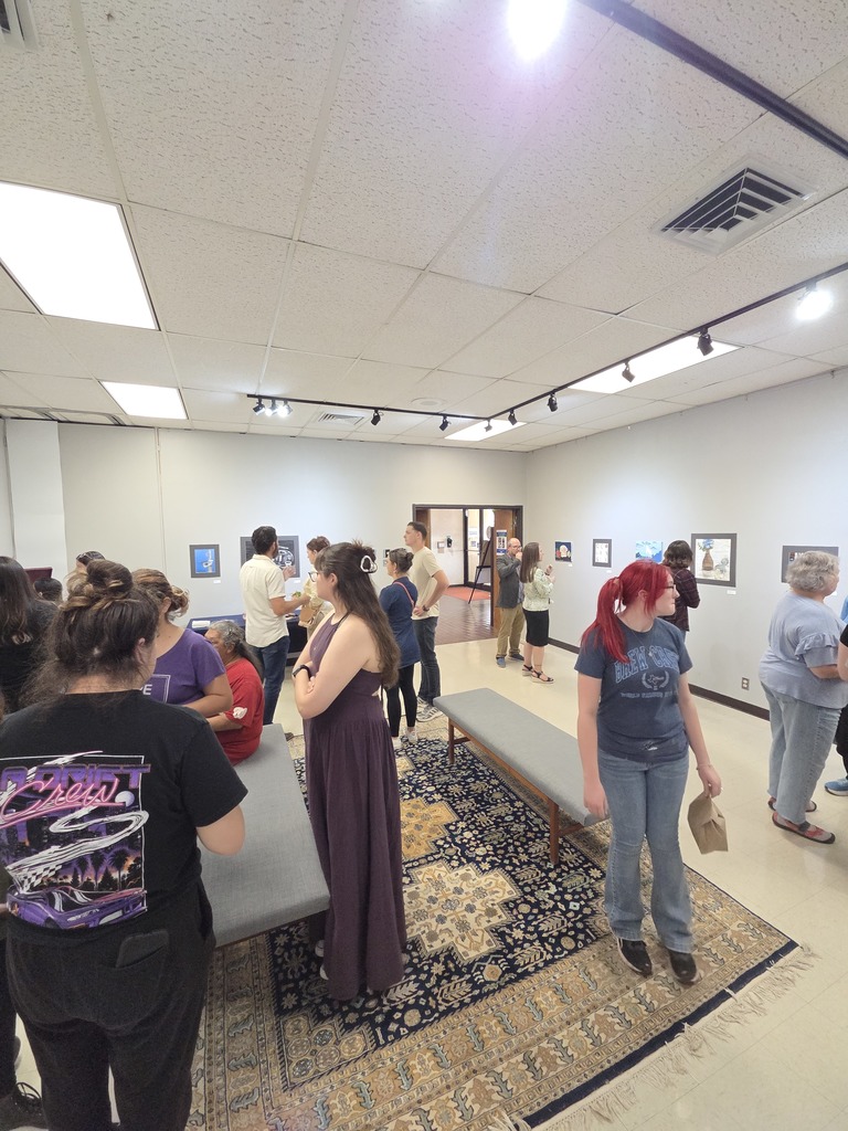 Students and community members gather inside gallery viewing displayed art pieces.