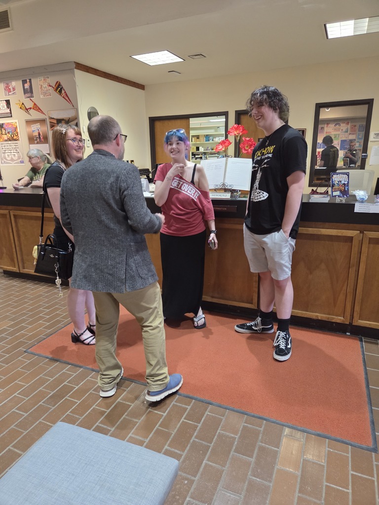 Students and staff visit in library lobby during campus art reception.