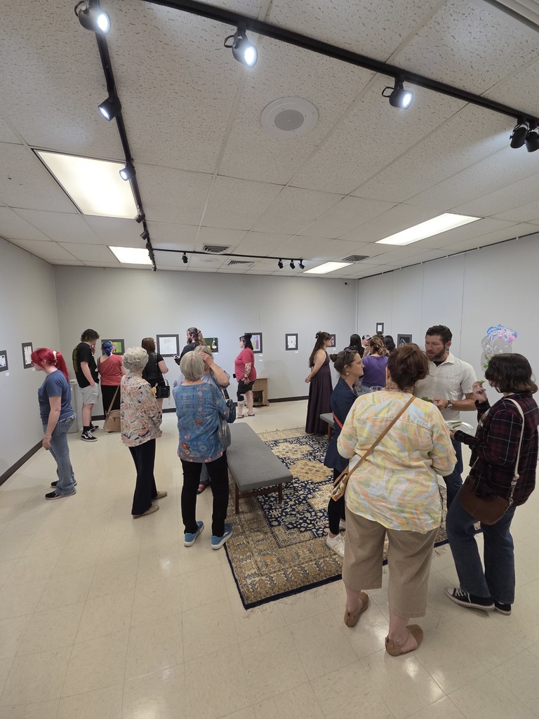 Visitors browse framed artwork during crowded campus gallery reception.