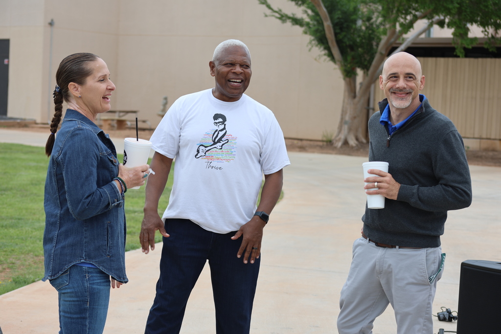 Faculty and staff laugh together holding drinks at outdoor gathering.