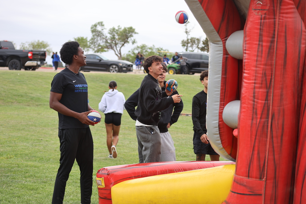 Students aim basketballs at inflatable hoop during campus activity day.
