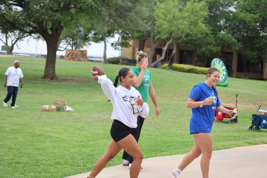 Student throws football while friends laugh during campus lawn games.