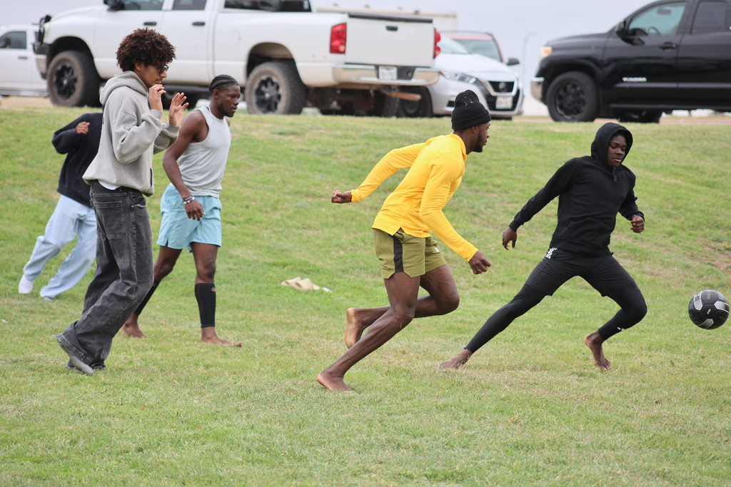Students race barefoot across grass during outdoor soccer game.