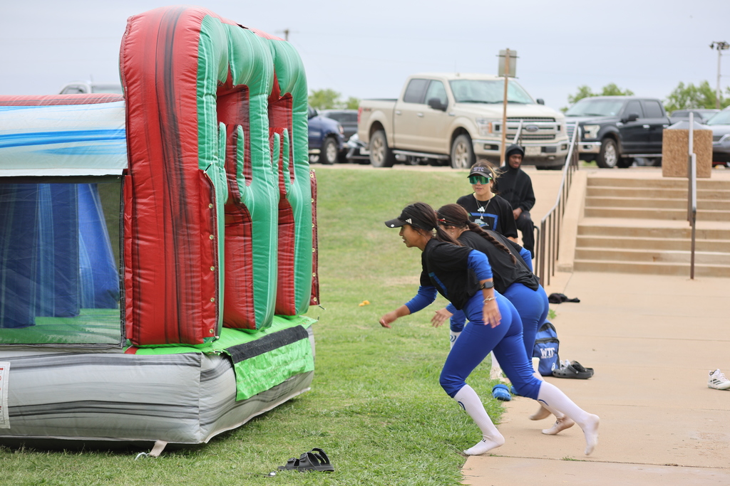 Softball players run toward inflatable obstacle during outdoor team challenge.