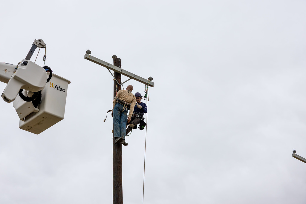 Student performing hurt man rescue work atop utility pole with bucket truck nearby.