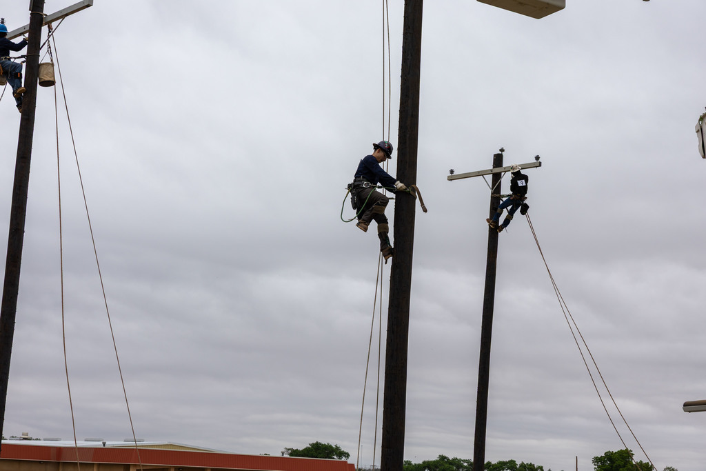 Two students climb separate utility poles during skills test.