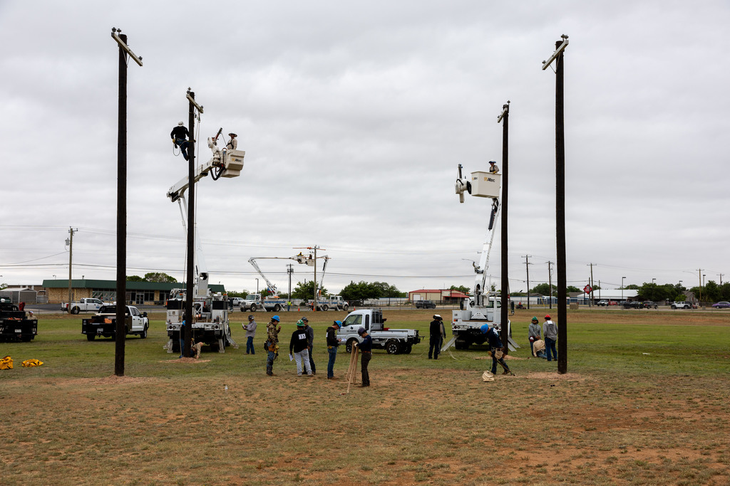 Wide view of students, utility poles, and bucket trucks at outdoor skills event.
