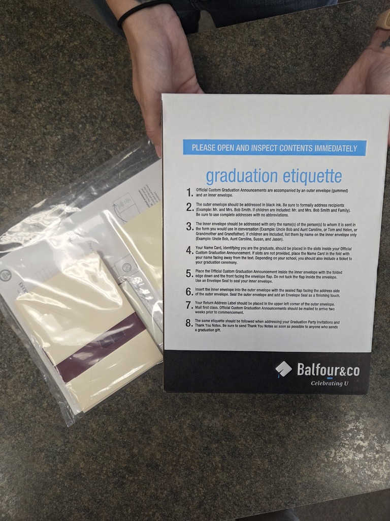 A pair of hands hold a box of graduation announcements. 