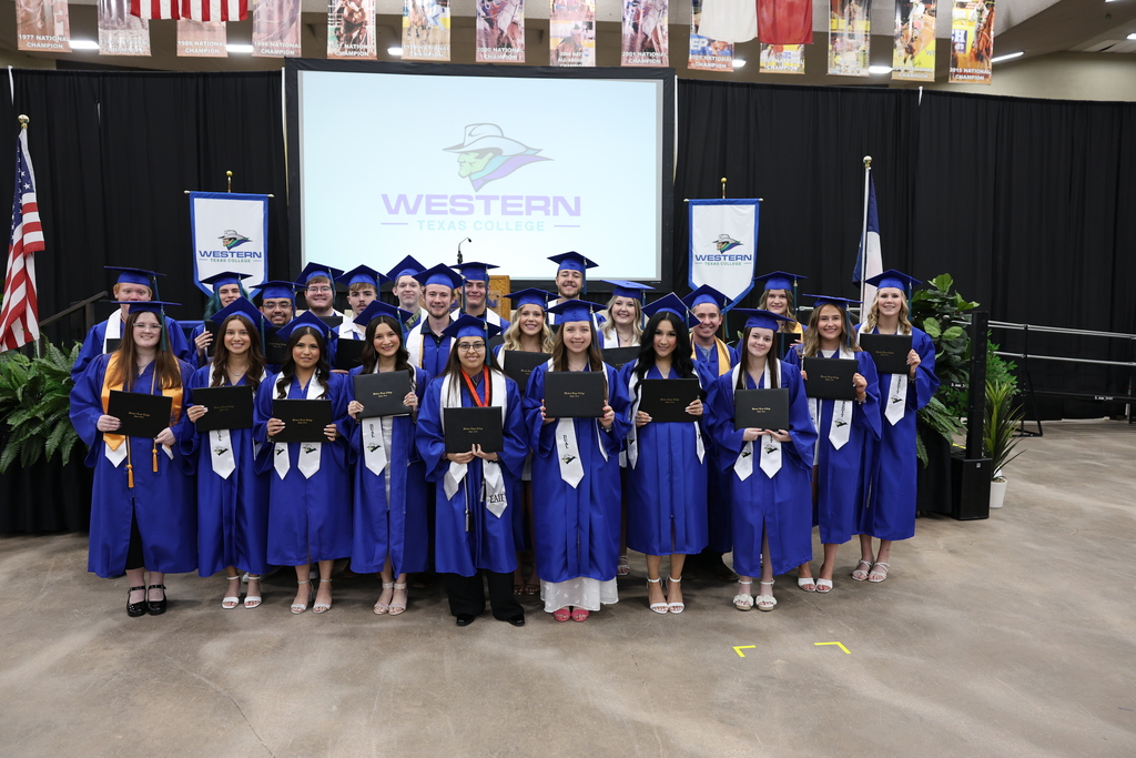 Group of graduates pose together holding diplomas in front of Western Texas College stage backdrop.