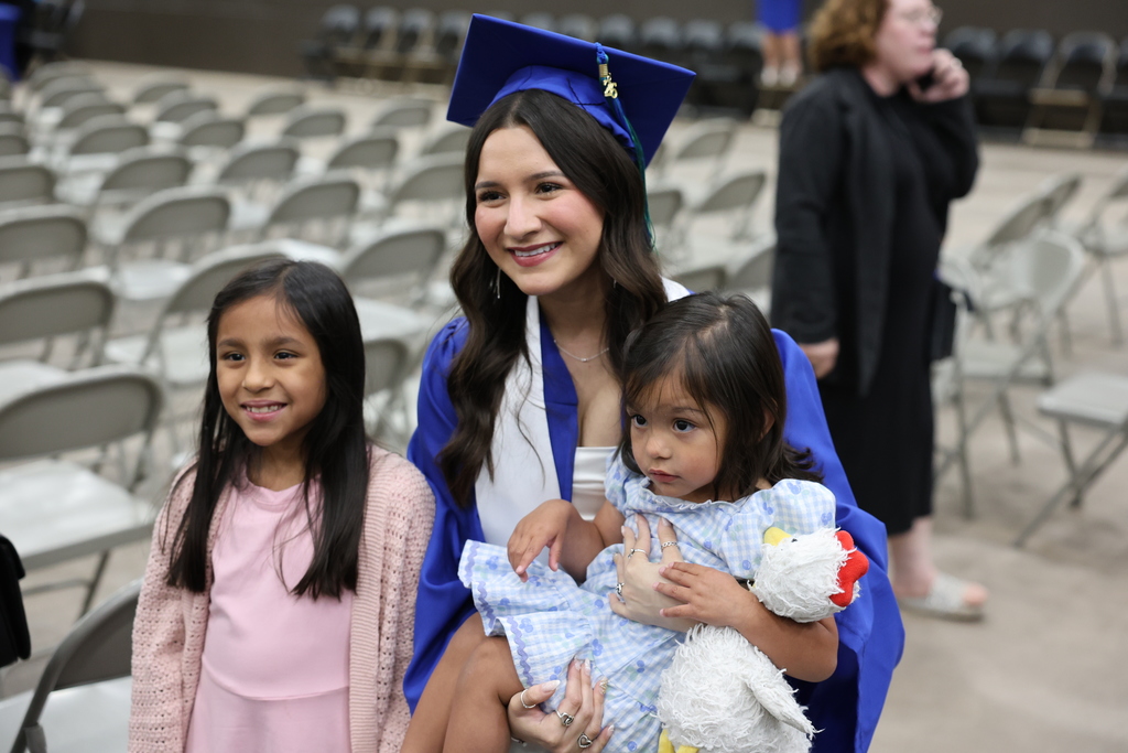 Graduate smiles while posing with two young children in arena seating area after ceremony.