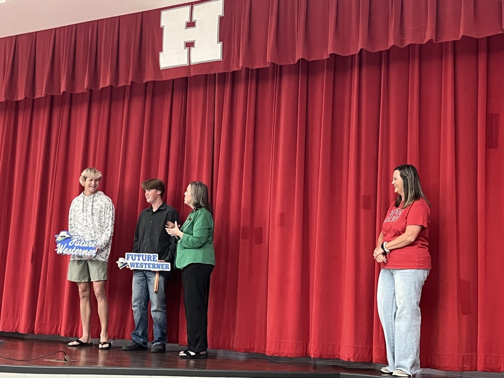 Markius McClure and Bradyn Lynch as Laura Caswell speaks and Alicia Anderson looks on while standing on stage.