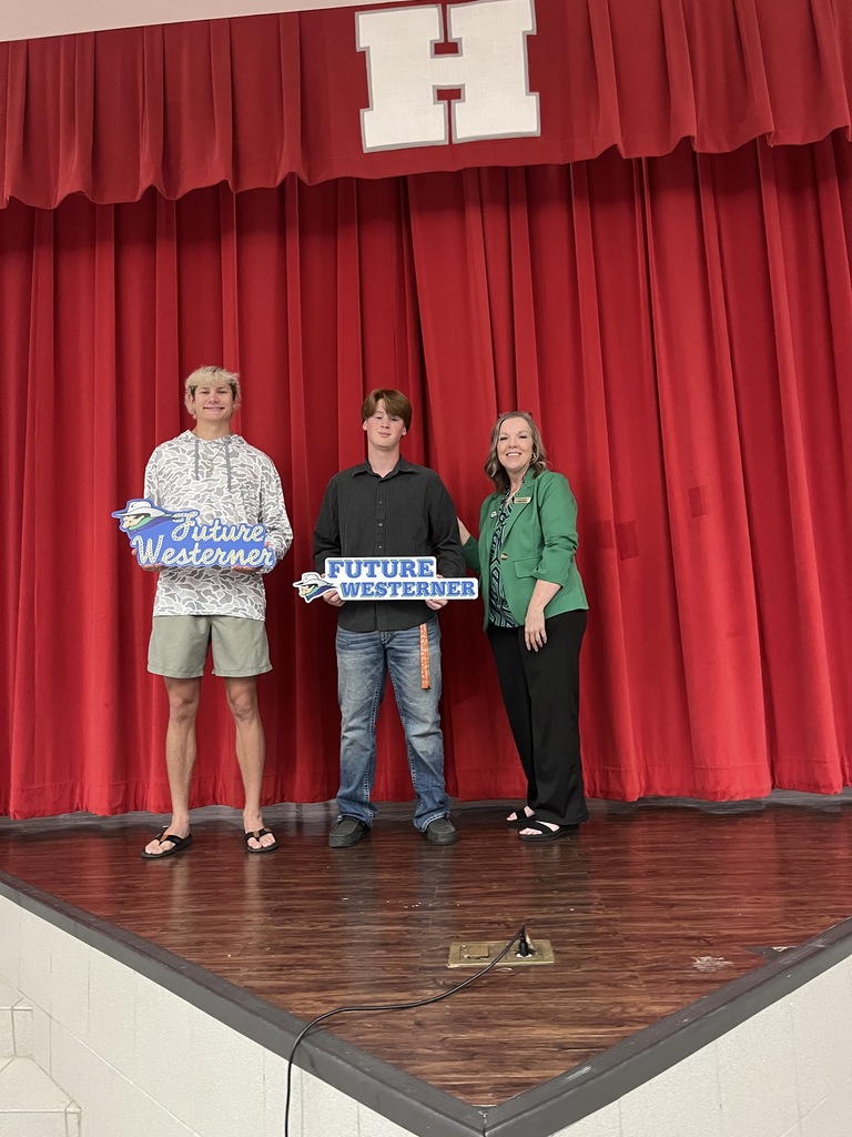 Markius McClure and Braidyn Lynch hold "Future Westerner" signs standing on a stage next Laura Caswell.