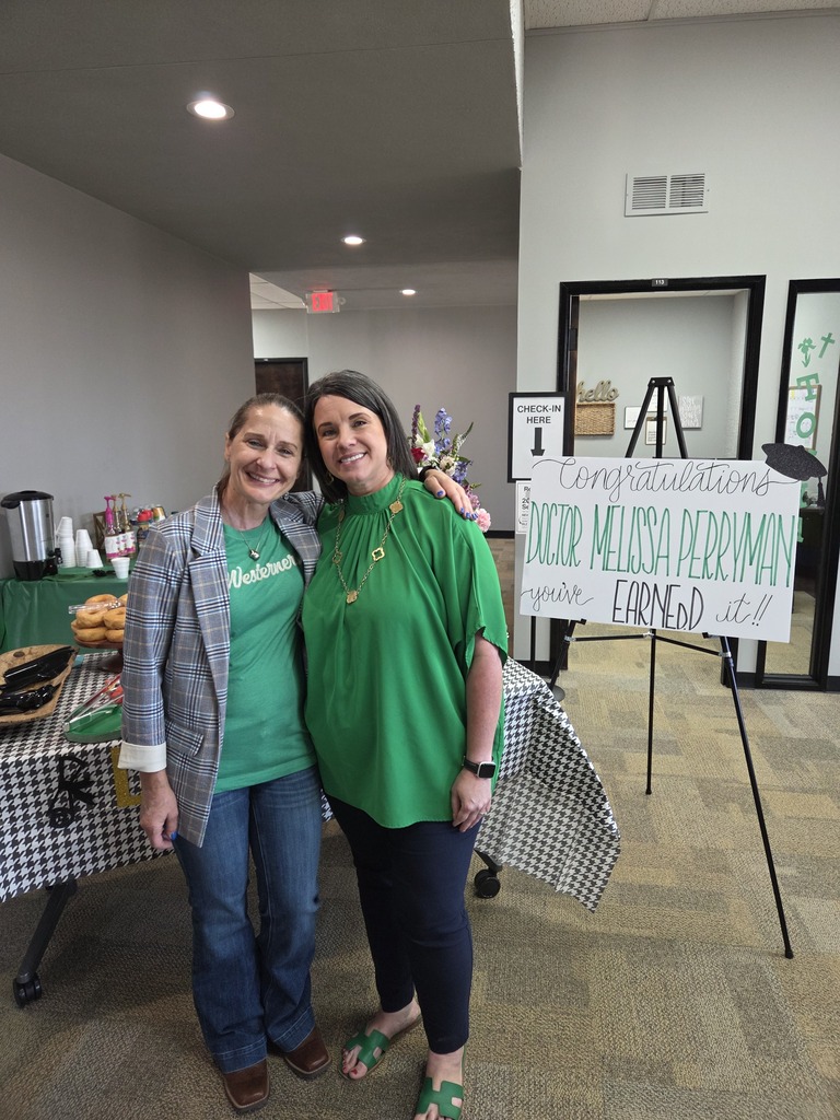 Dr. Sharp and Dr. Perryman pose with their heads together standing next to a congratulations poster.