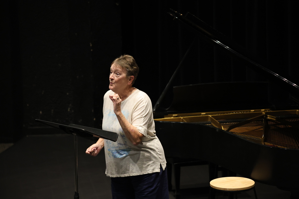 Dr. Alesio rehearses leaning forward in front of a grand piano on stage.
