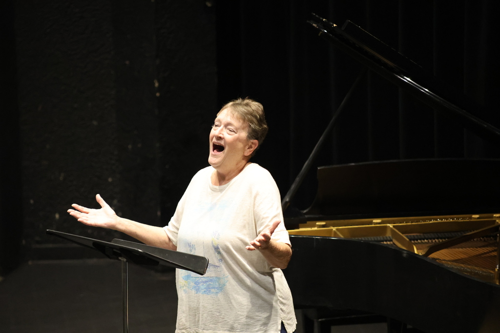 Dr. Alesio rehearses with arms out  in front of a grand piano on stage.