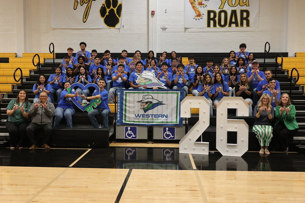 A group of students wearing Western Texas College t-shirts making a "w" with their hands sits in bleachers smiling with WTC employees on the front row.