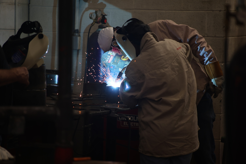 Welding students practice techniques in lab while sparks fly from active welding project.