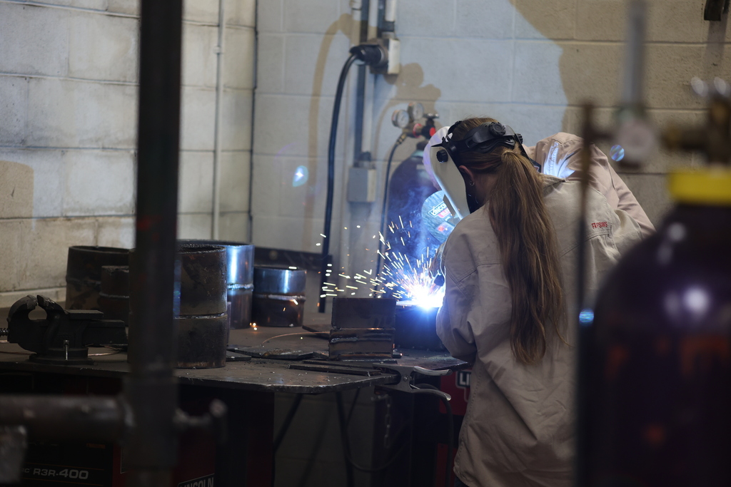 Student welds metal project in training lab while instructor provides guidance nearby.