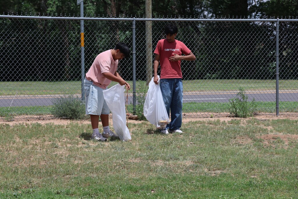 Students pick up trash near campus fence line during cleanup project.