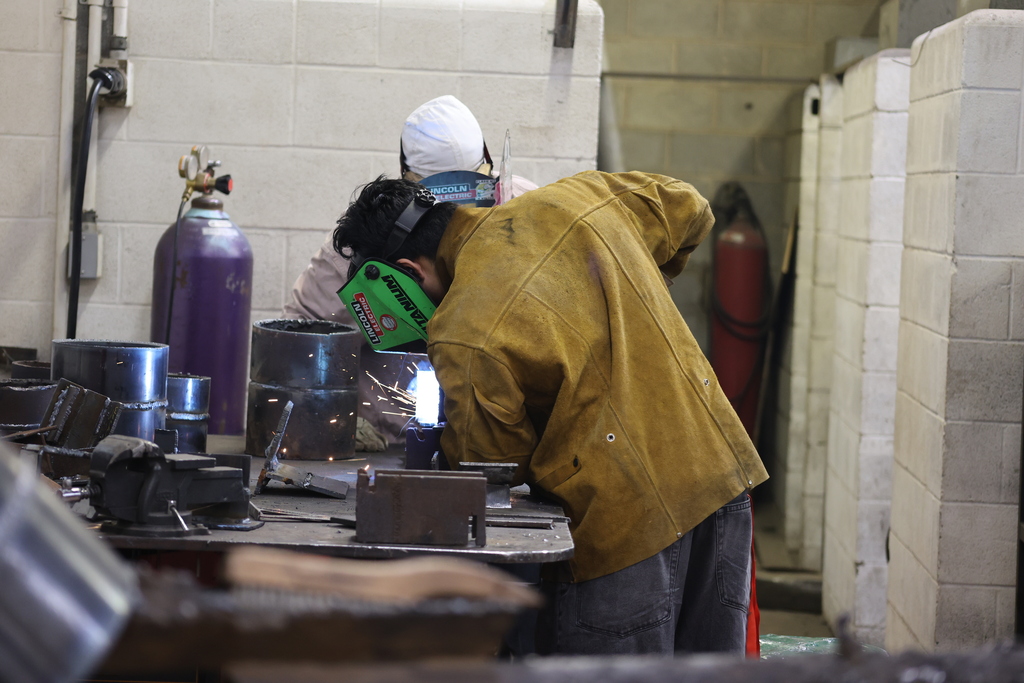 Welding students practice metal fabrication skills in a campus lab under instructor supervision.