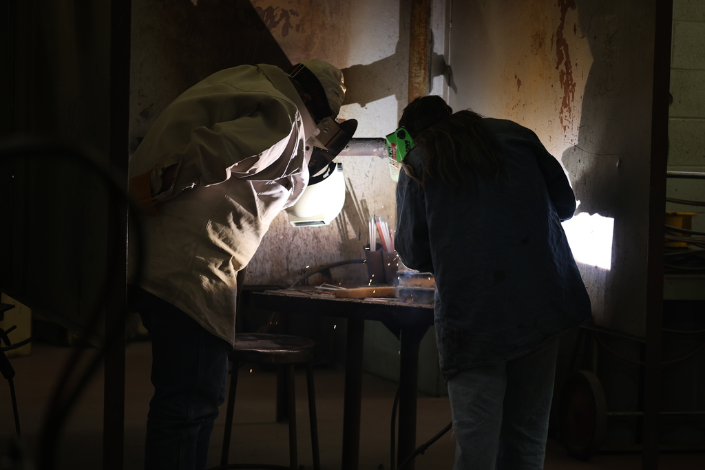 Welding students work together in a welding booth during hands-on training.