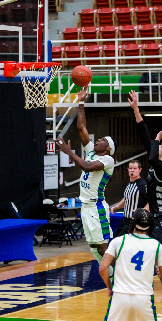 Basketball player in a Western Texas College uniform drives toward the basket for a layup during a game while defenders and a referee watch the play.