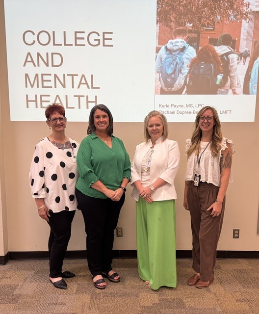 Four professional women stand in fornt of a screen that reads "College and Mental Health."