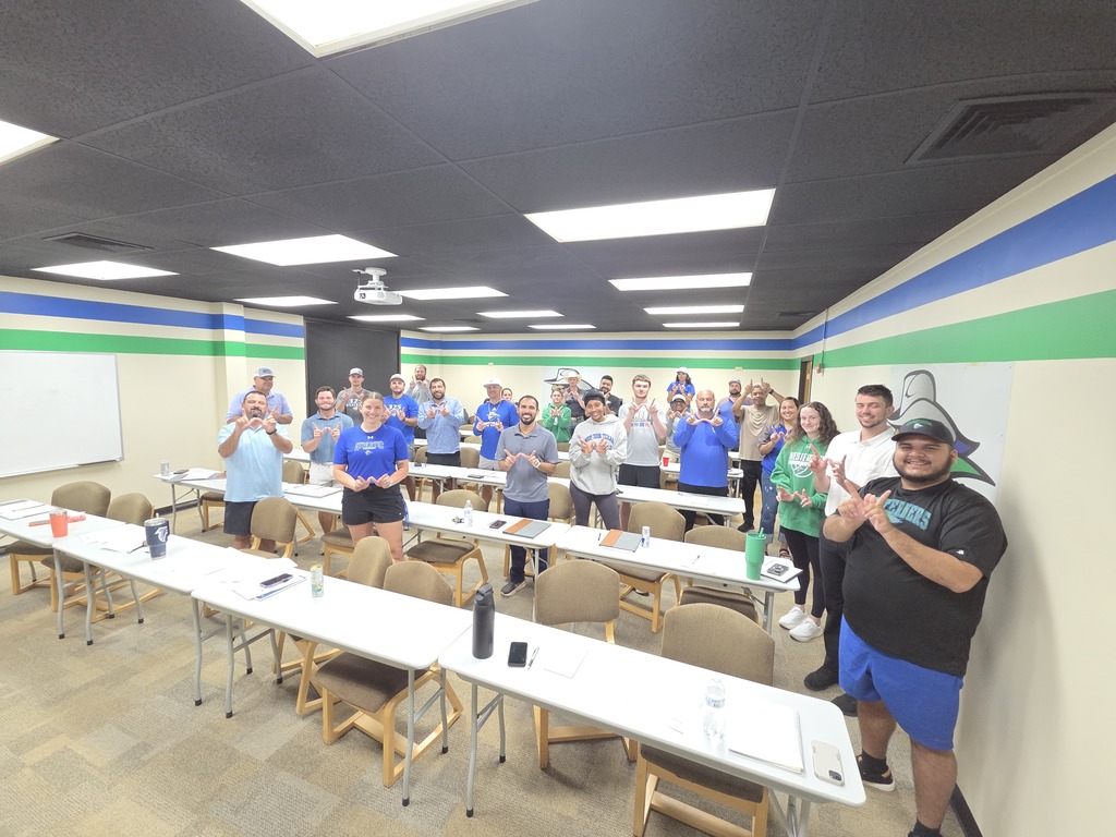 Faculty and staff pose together in a Western Texas College classroom, making the Westerner hand sign during employee training.