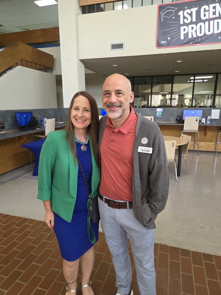 Two Western Texas College employees pose together in the campus lobby beneath a First-Generation Proud banner.