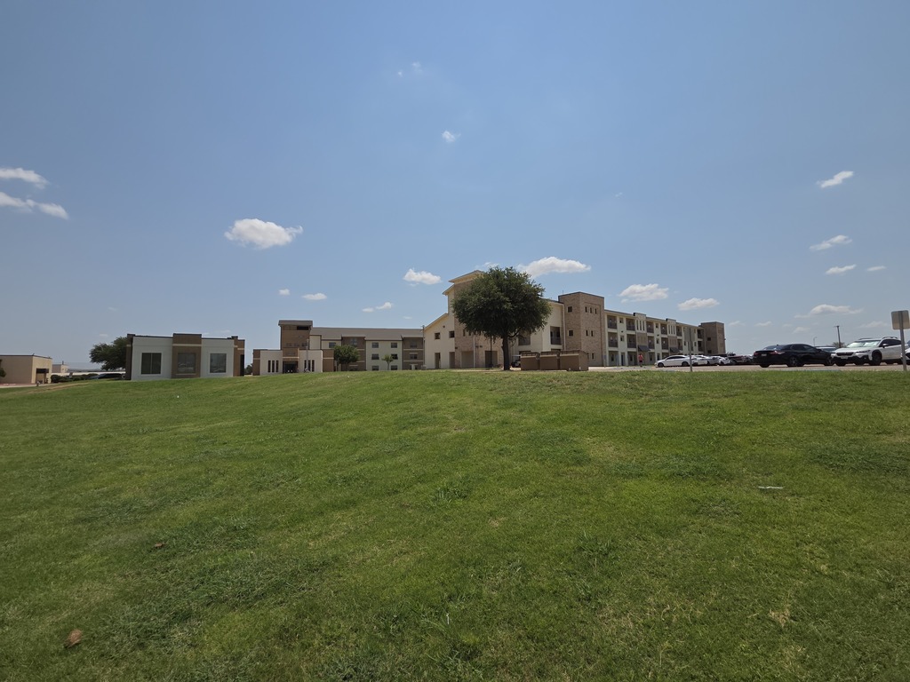 Western Texas College residence halls stand beyond a grassy lawn under a bright blue sky with scattered clouds.