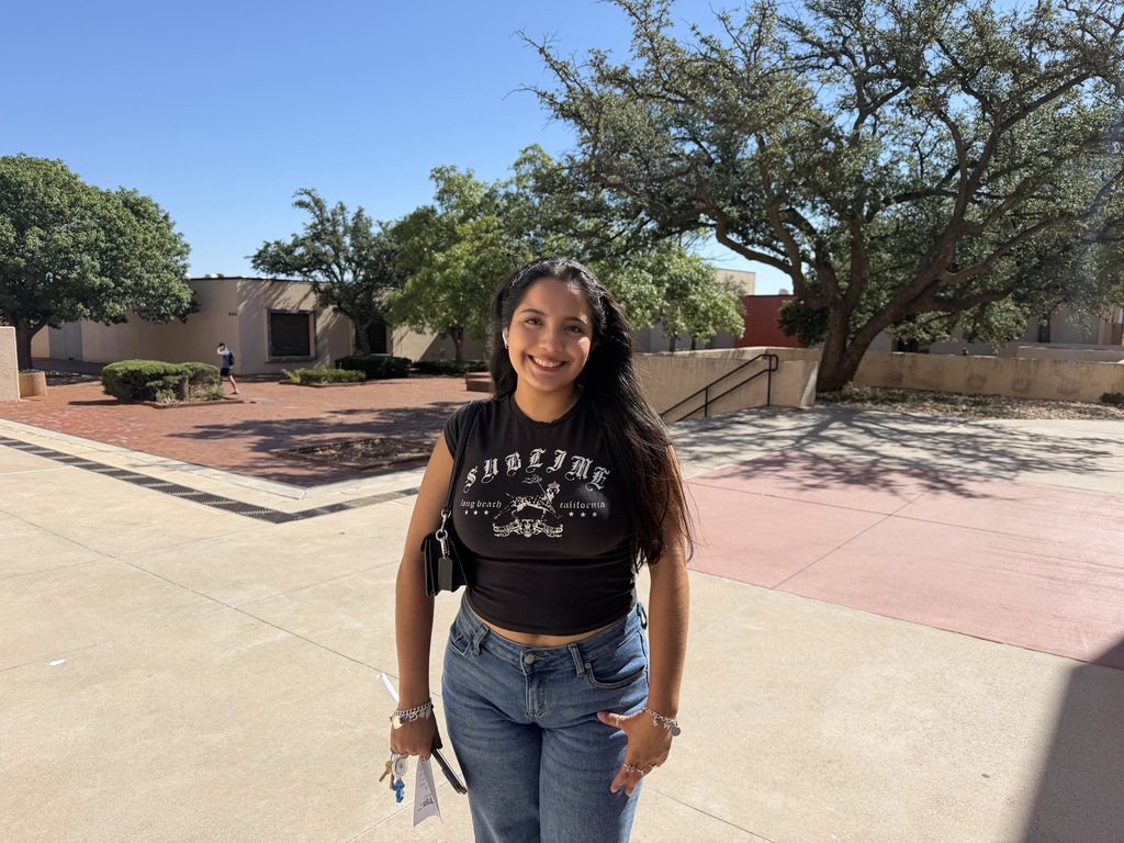 A WTC student smiles while standing outside among campus buildings and trees.