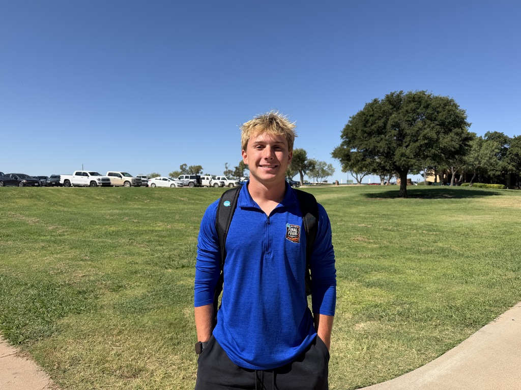 A WTC student wearing a backpack smiles on a grassy area of campus.