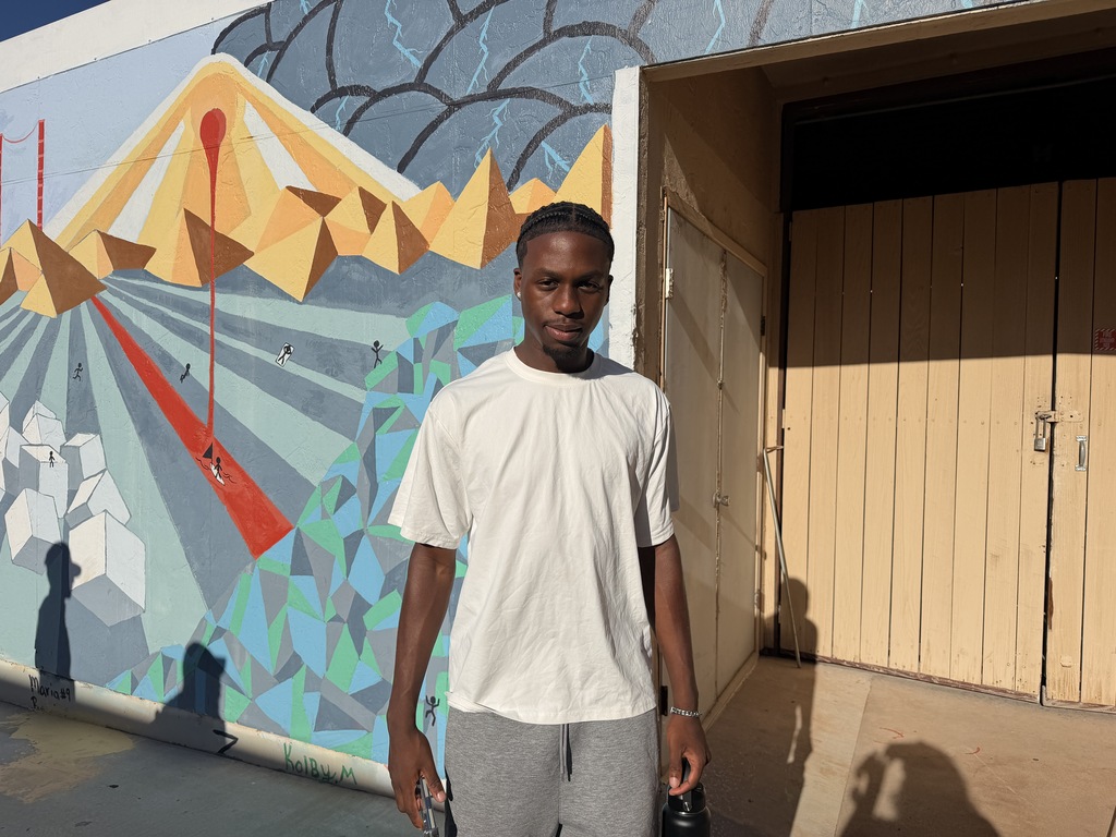 A WTC student stands in front of a colorful outdoor mural on campus.