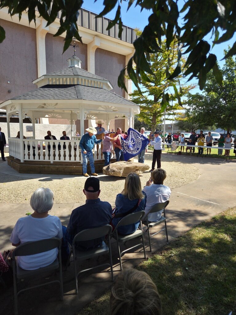 Community leaders unveil a Scurry County 150th anniversary marker as attendees watch near the gazebo.