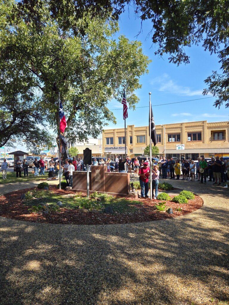 Community members gather around the Scurry County memorial and flags during an outdoor 150th anniversary ceremony.