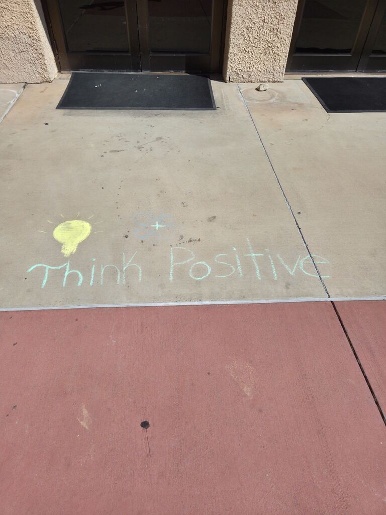 Colorful chalk drawings and the words Think Positive decorate a sidewalk outside a WTC campus building.