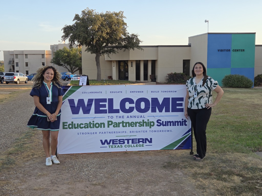 Two women stand on either side of a "Welcome" banner.