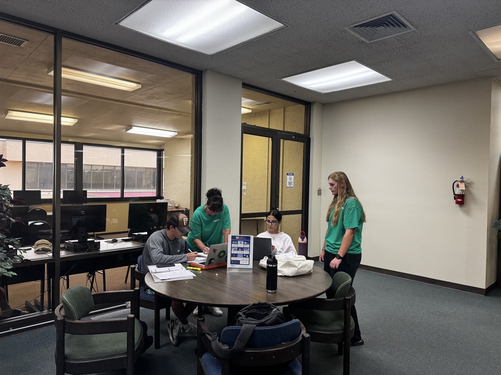 Tutors wearing tutoring shirts help students sitting at a table.