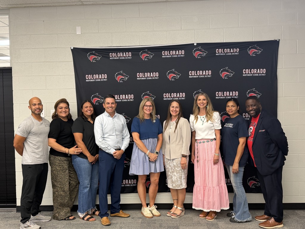 Smiling Colorado ISD Board members stand with Dr. Sharp and Molli Fleming with a Colorado ISD banner behind them.