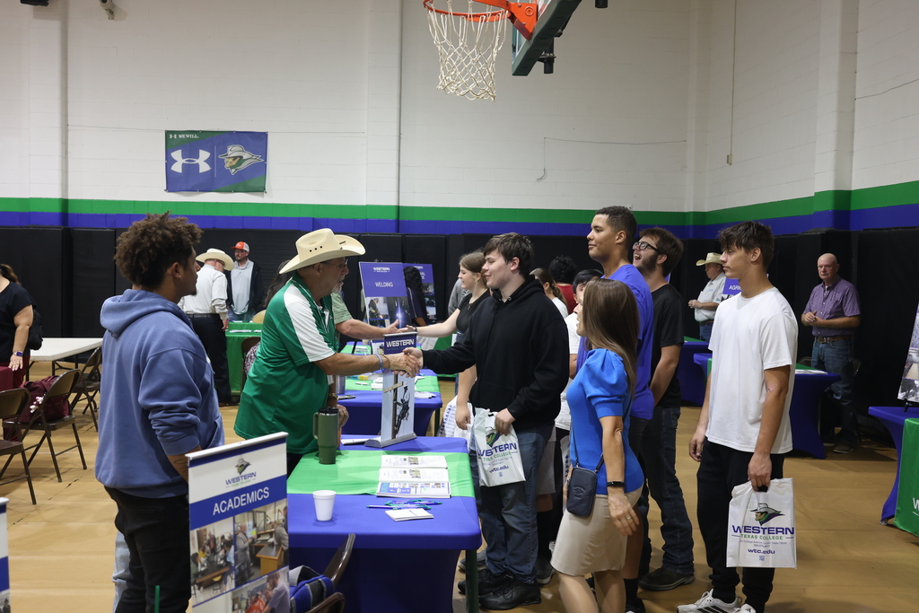 A Western Texas College representative greets a student while other students wait at an information table during the WTC College Fair.