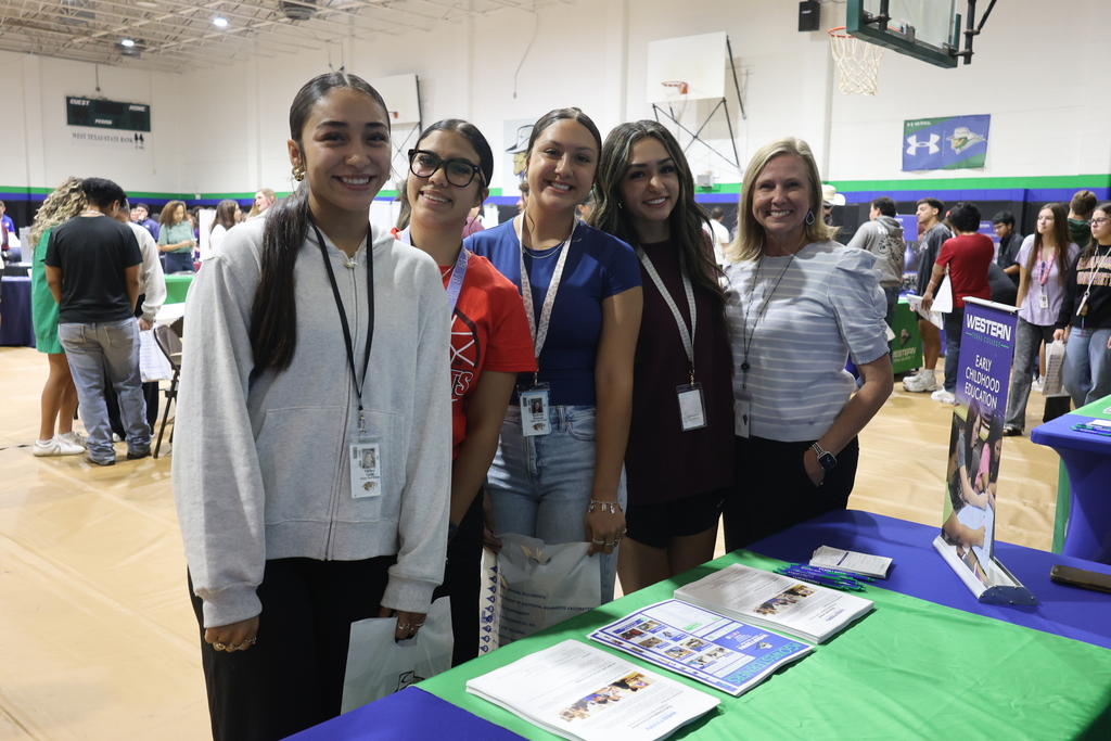 Four students and a Western Texas College representative smile for a photo beside the Early Childhood Education information table at the WTC College Fair.