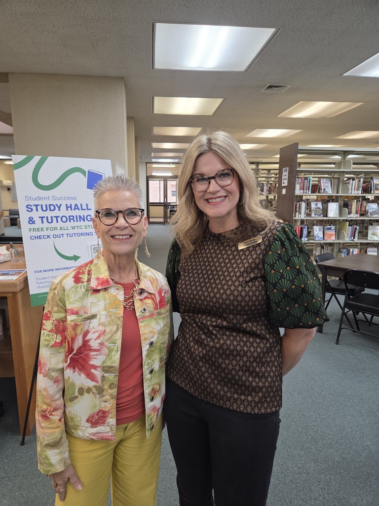 Two women pose together near the Student Success Study Hall and Tutoring poster in the WTC Resource Center.