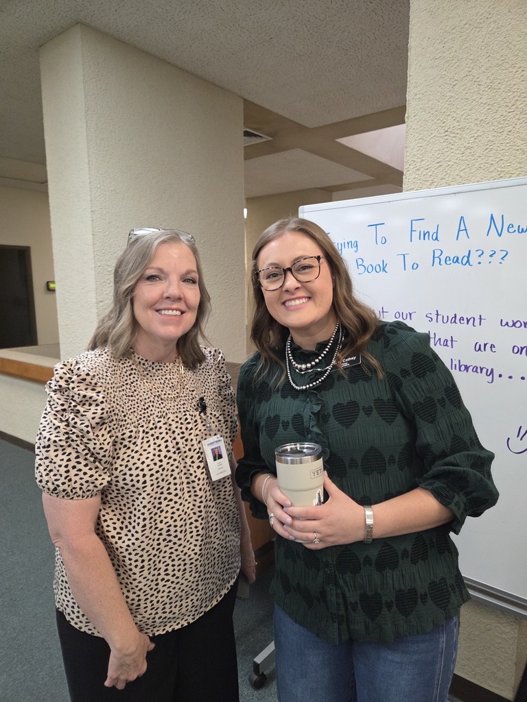 Two people smile together near a library display during Coffee with the Chamber.