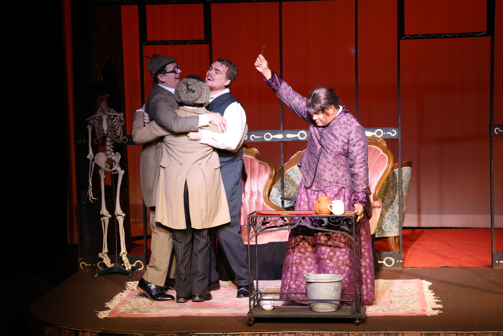 Three actors group hug as another actor holds up a key on stage during a rehearsal for the play.