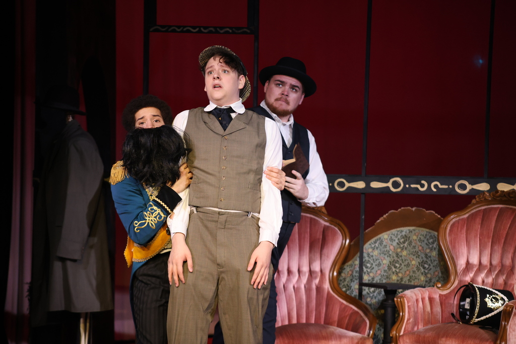 Three actors looking frightened  perform a scene from the play on stage.