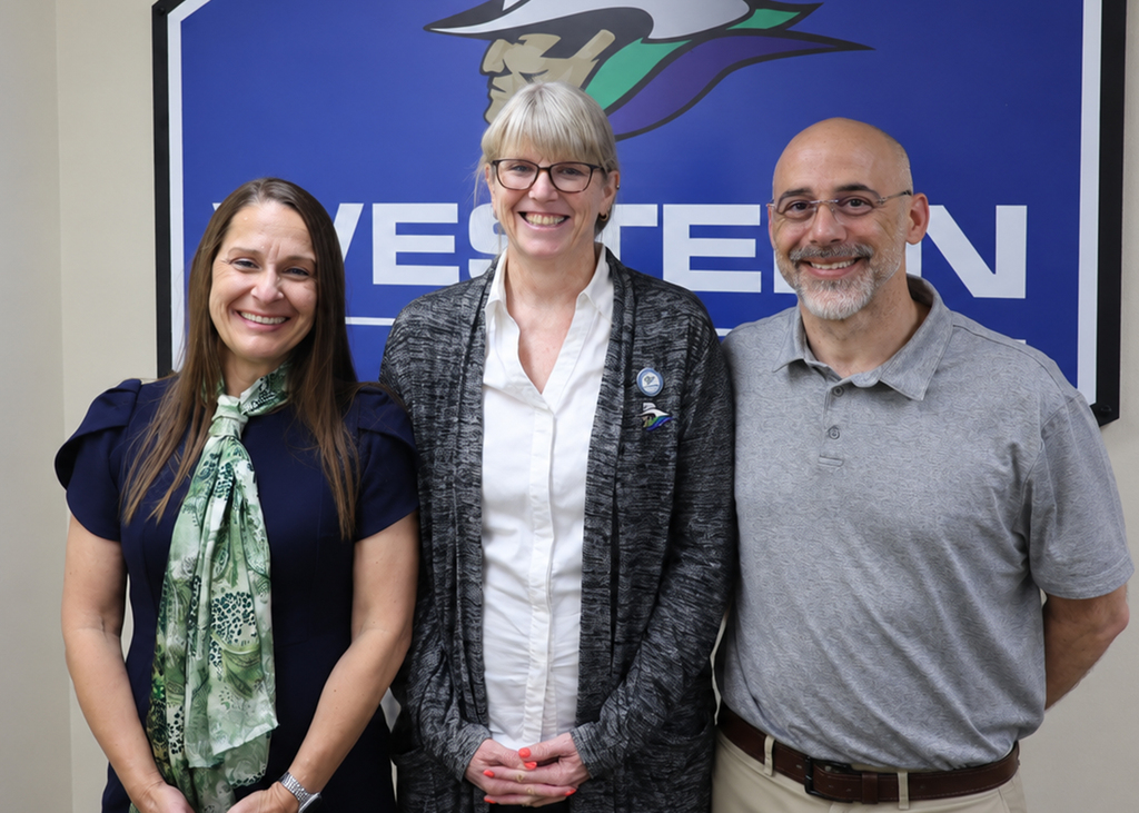 Dr. Laurie Sharp, Stephanie Ducheneaux, and Dr. Don Sewell stand smiling in front of a sign with the college logo on it.