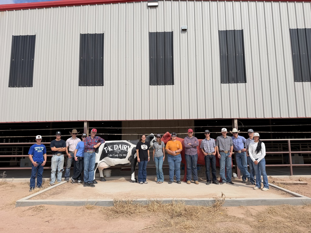 Western Texas College students and a dairy farm representative pose outside a barn beside a cow statue.