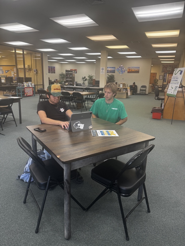 A tutor helps a student sitting at a table in the Library.